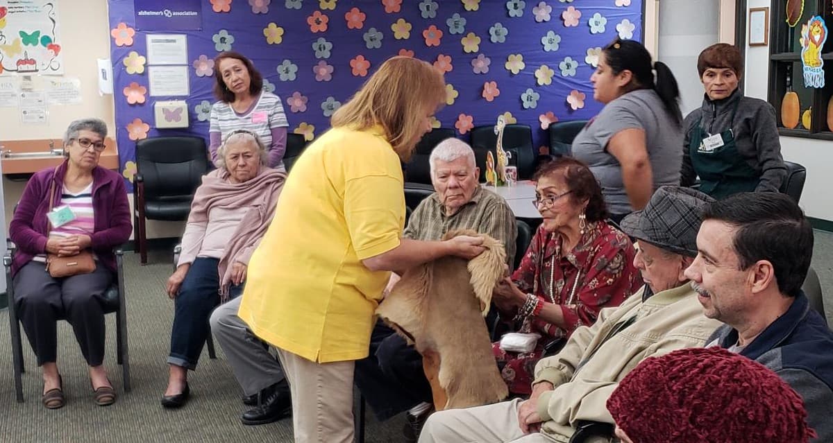 Docent holds an animal pelt as a seated woman touches it with her hands