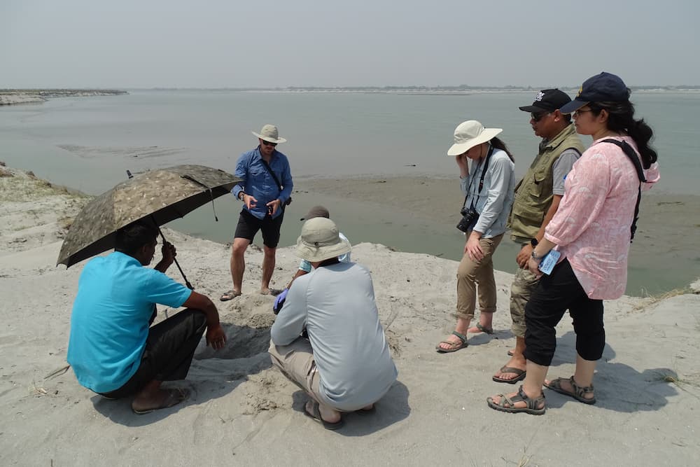 A group of scientists ground around a patch of white sand.