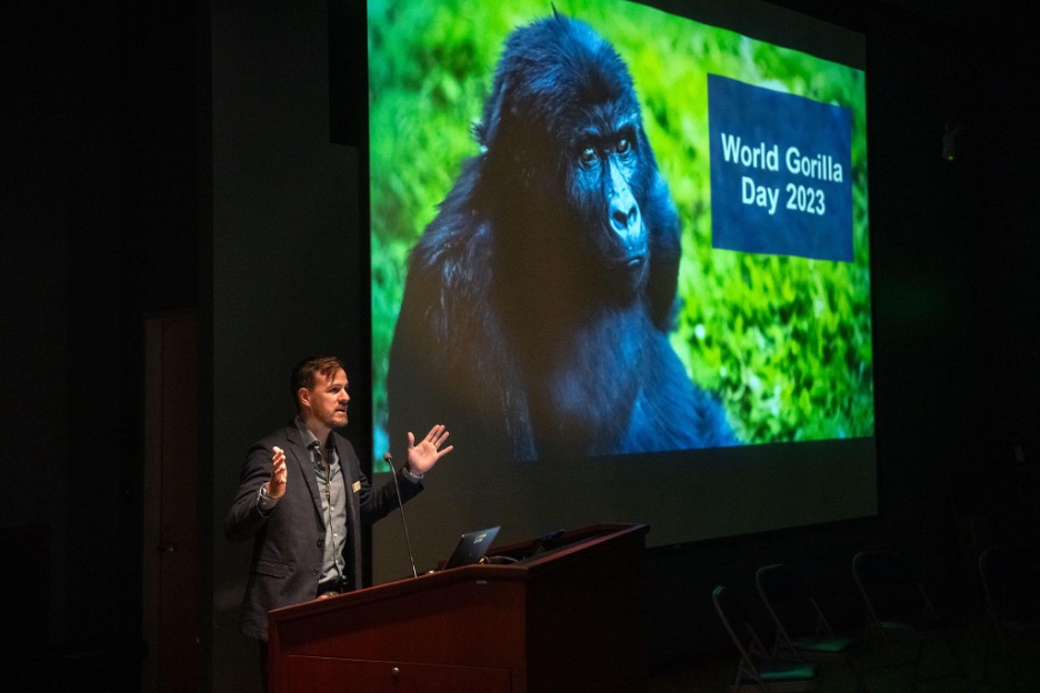 Standing at a lectern, Dr. Jake Owens, L.A. Zoo Director of Conservation, opens ‘Gathering for Gorillas’ event on Saturday, Sept. 23, 2023. An image of a Grauer's gorilla and the text "World Gorilla Day" are projected on a screen behind him.