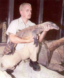 Ian Recchio adopts a wide stance as he holds a young Komodo in both arms.