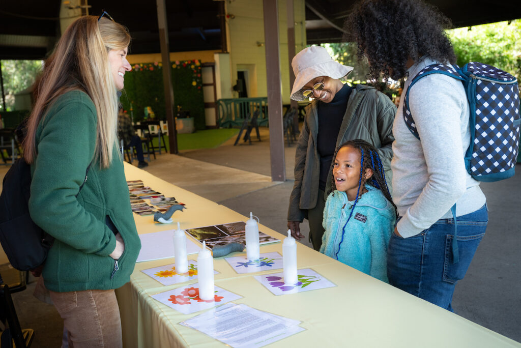 A smiling woman engages with a family at a table with educational materials.