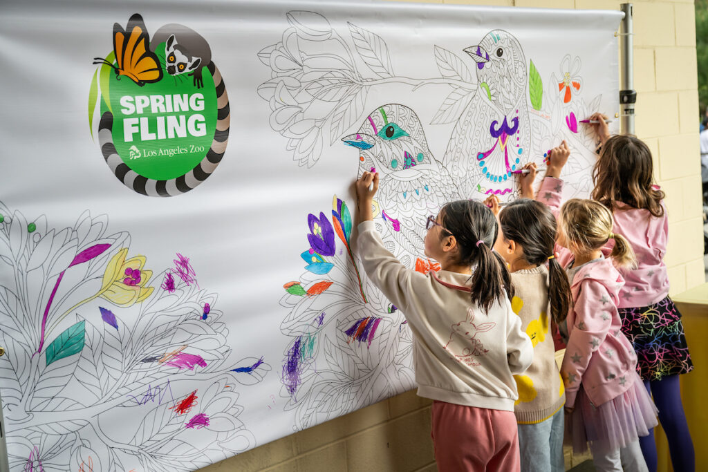 A group of children colors a large nature-themed mural at an event.