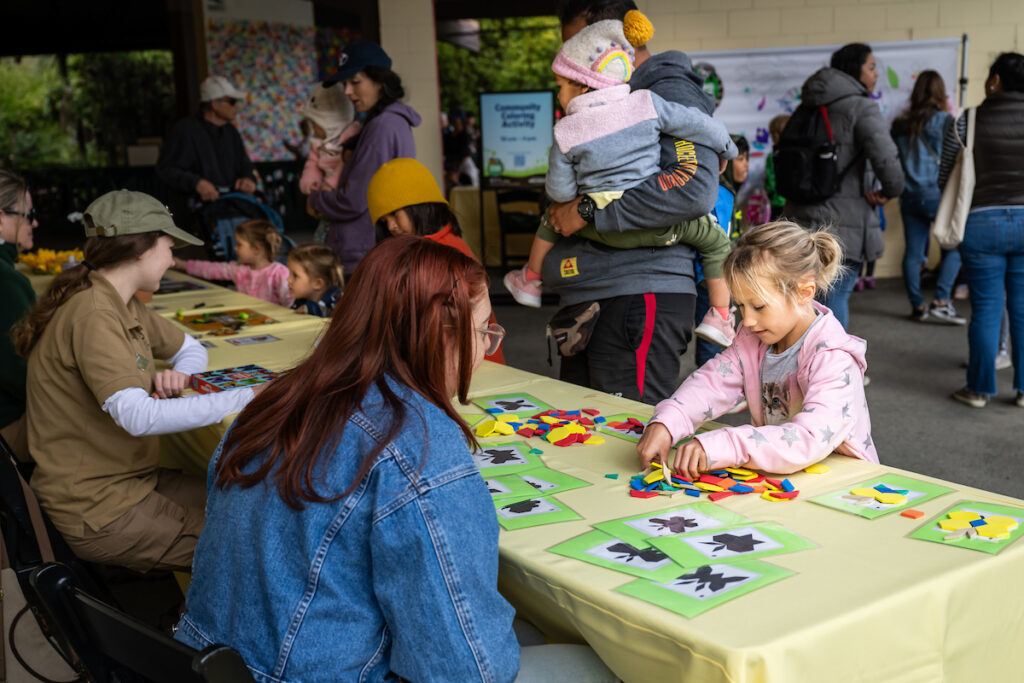 A young girl assembles colorful shapes at a table during an interactive event.