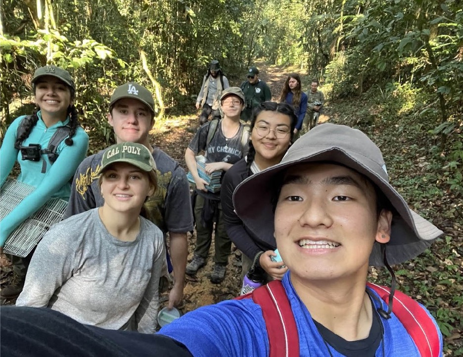 A group of students stops for a selfie on a leafy forest trail.