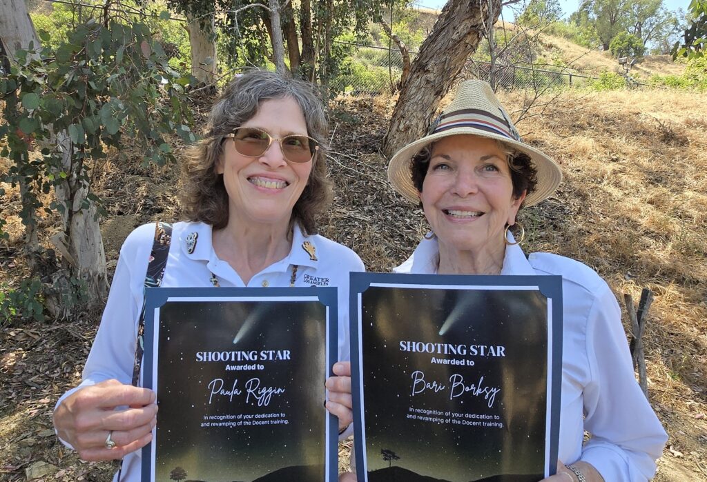Bari Borsky and Paula Riggin photographed holding up thee Shooting Star awards. Wearing GLAZA uniforms with a wooded background.