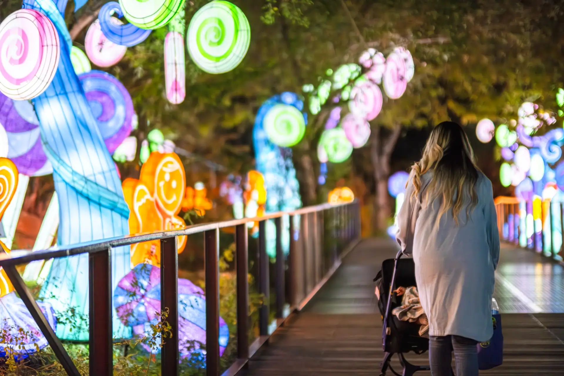 woman pushing a stroller along a pathway flanked with holiday light displays