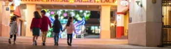 children holding hands and walking beneath strands of string lights